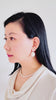 Asian woman with black hair and fair skin wearing the Statement set with a Statement baroque earrings and the date night necklace. She's wearing a cream color top. She flicks the earrings and it shines and moves with the luster. It's beautiful.